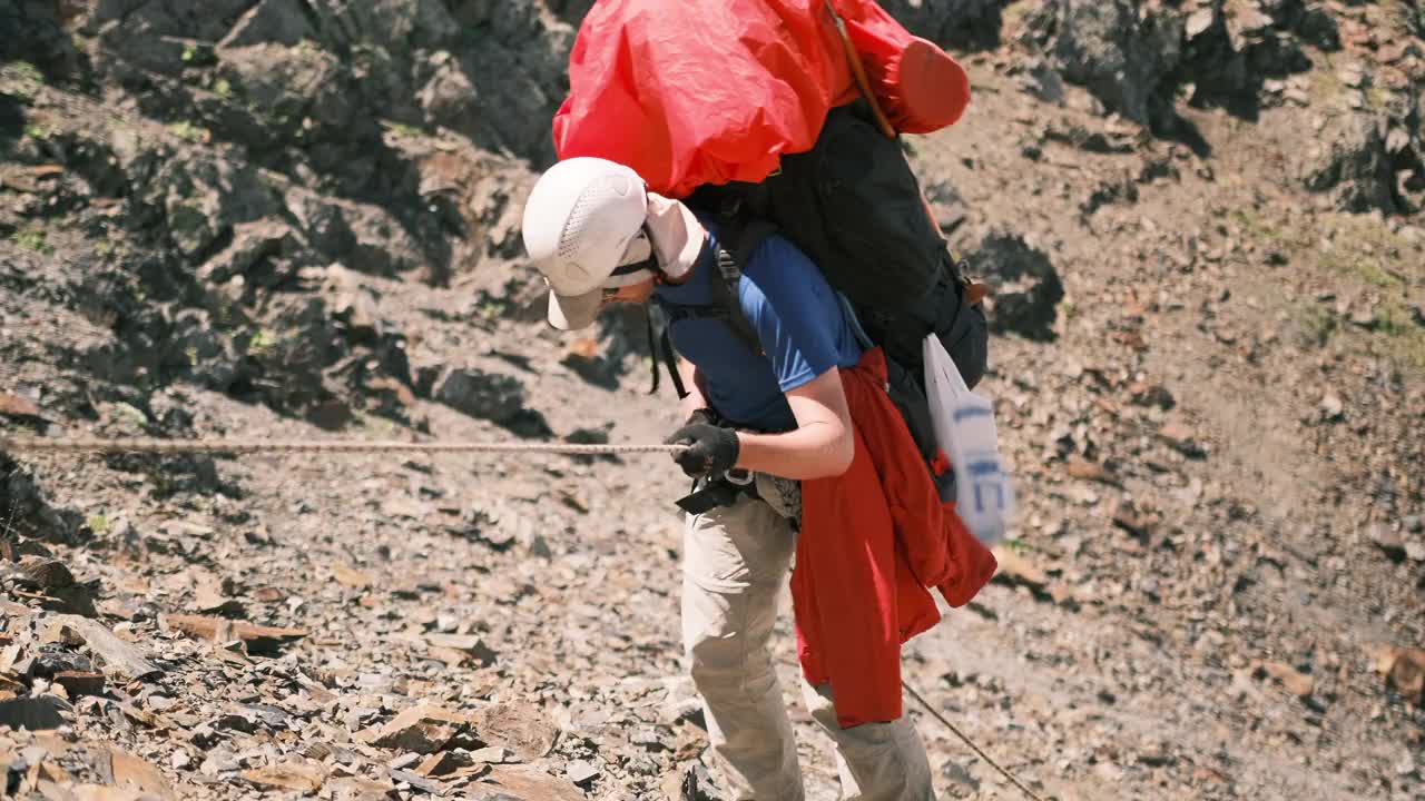 一名登山者背着背包，借助带有保护系统的绳索下山。视频素材