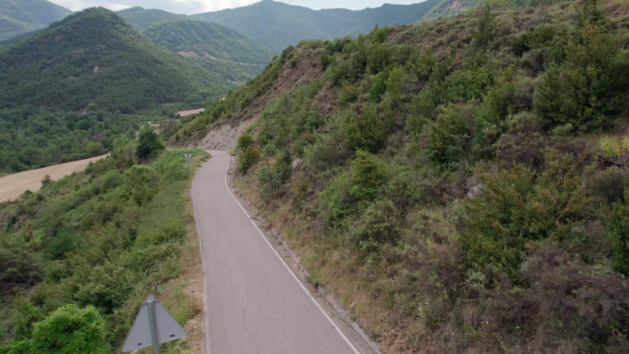 美丽的无人机视野的沥青公路在高山上。山脉消失在天空中，天空有些许阴云，但山峰被阳光照亮。视频素材