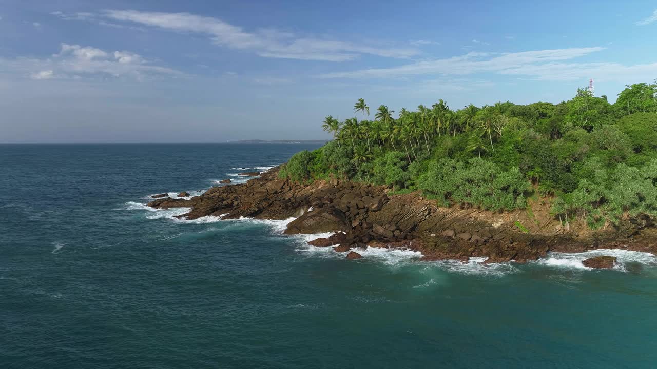 接近岩石峭壁接近一个多岩石的半岛。绕着石头海角飞行。海浪拍打在石崖上。悬崖上覆盖着茂密的丛林视频素材