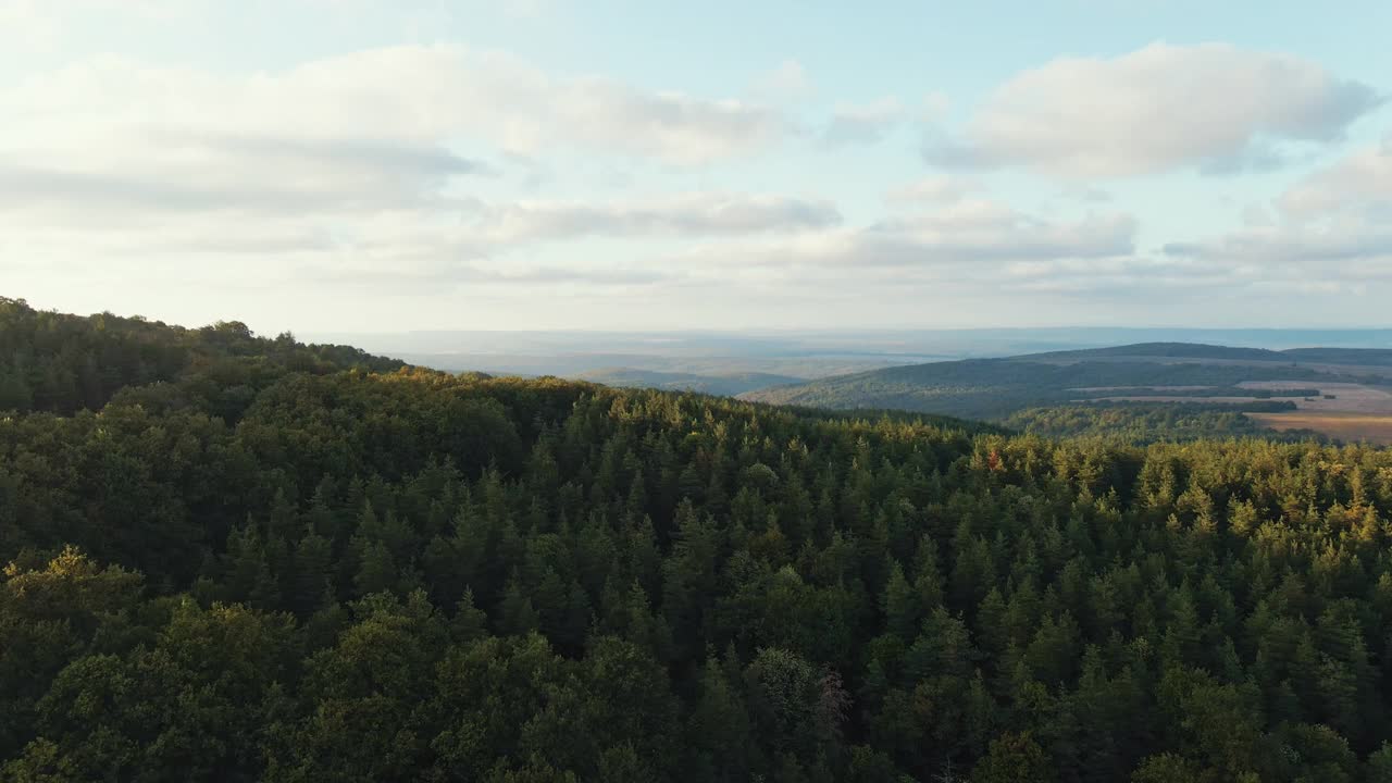 夏天阳光明媚的日子里的山脉鸟瞰蓝天上的云朵无人机滑行。太阳射线。山坡上有绿色的松林。蓝色天空中的一轮太阳缓缓落在山顶。自然视频素材