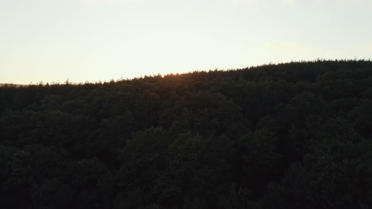 镜头光晕在山在橙色日落在夏天早晨航拍无人机。太阳射线。山坡上有绿色的松林。蓝色天空中一轮明亮的太阳慢慢地落在山顶上。自然视频素材