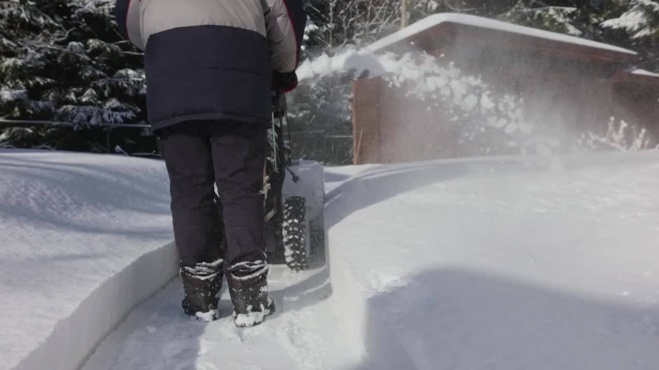 有人用吹雪机清扫人行道上的积雪。暴风雪过后，冬日阳光明媚的乡间小屋。视频素材