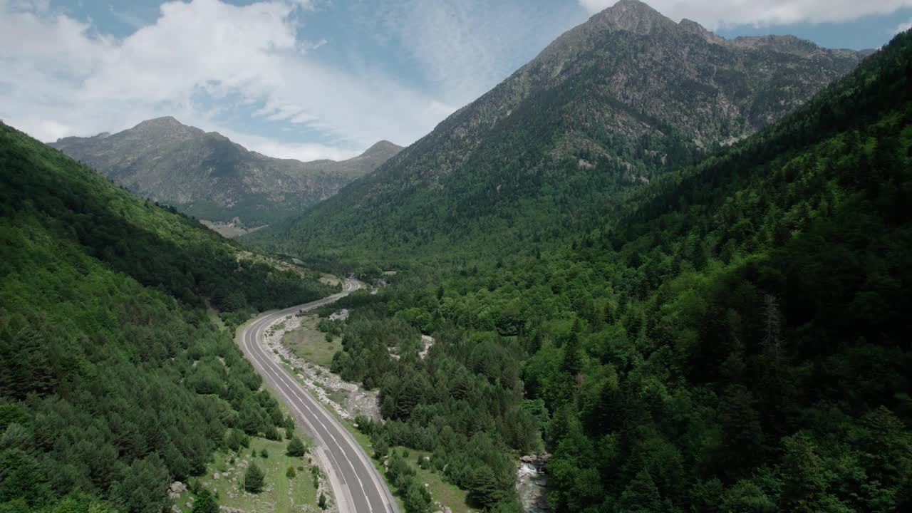 美丽的无人机视野的沥青公路在高山上。山脉消失在天空中，天空有些许阴云，但山峰被阳光照亮。视频素材