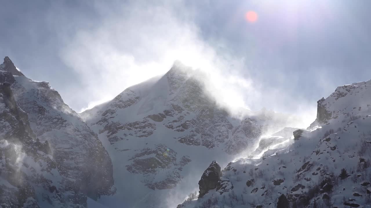 在长焦镜头上的时间流逝，高山的雪峰被风吹起的雪。山区恶劣的天气条件视频素材