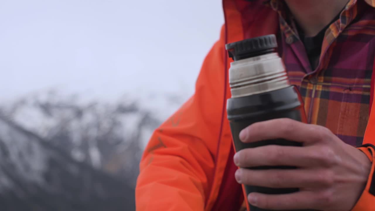 在高加索雪山的映衬下，一个特写镜头中的男子将热茶从保温瓶中倒进杯子里。旅行中温暖和舒适的概念。视频素材