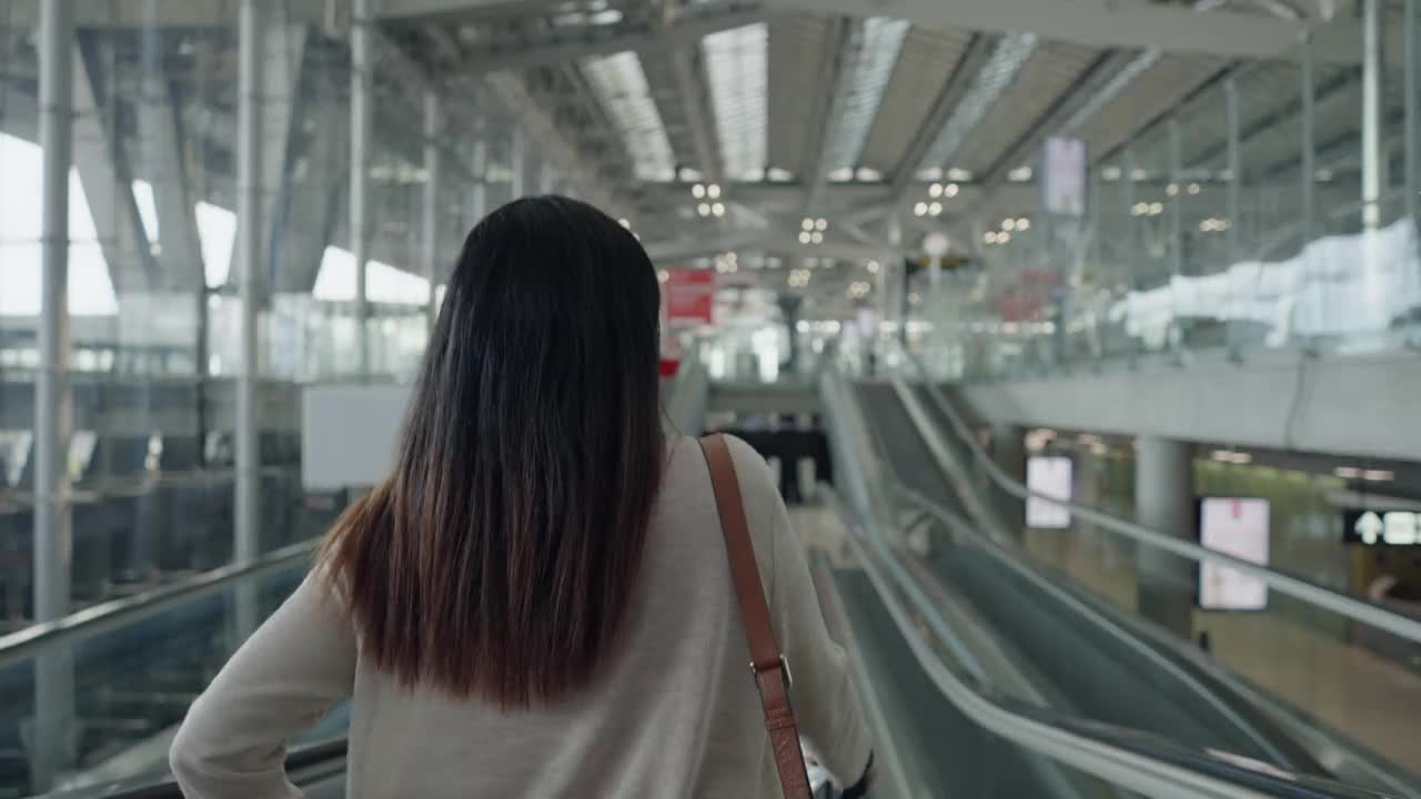 亚洲女性旅客在机场带着行李，护照，机票，一个新的旅程，旅行，度假在自动扶梯上，后面的视图视频素材