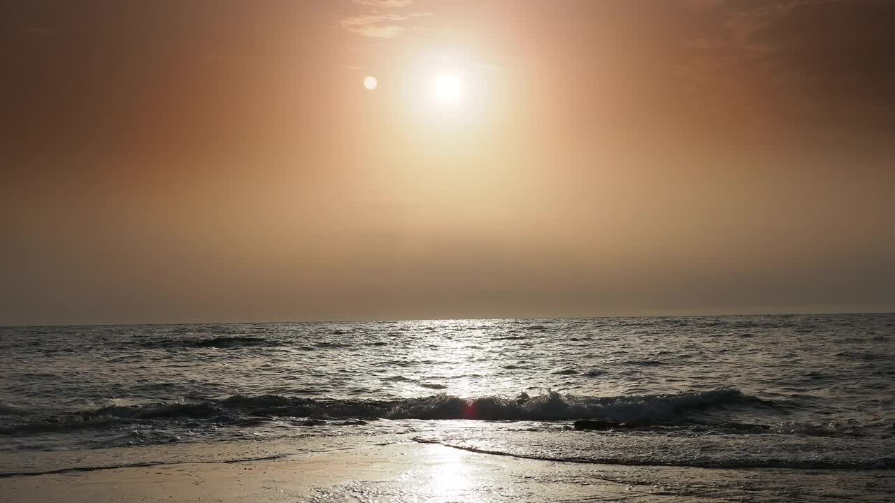 日出时的海岸线景观，太阳在地平线上，海浪拍打着海岸。视频素材