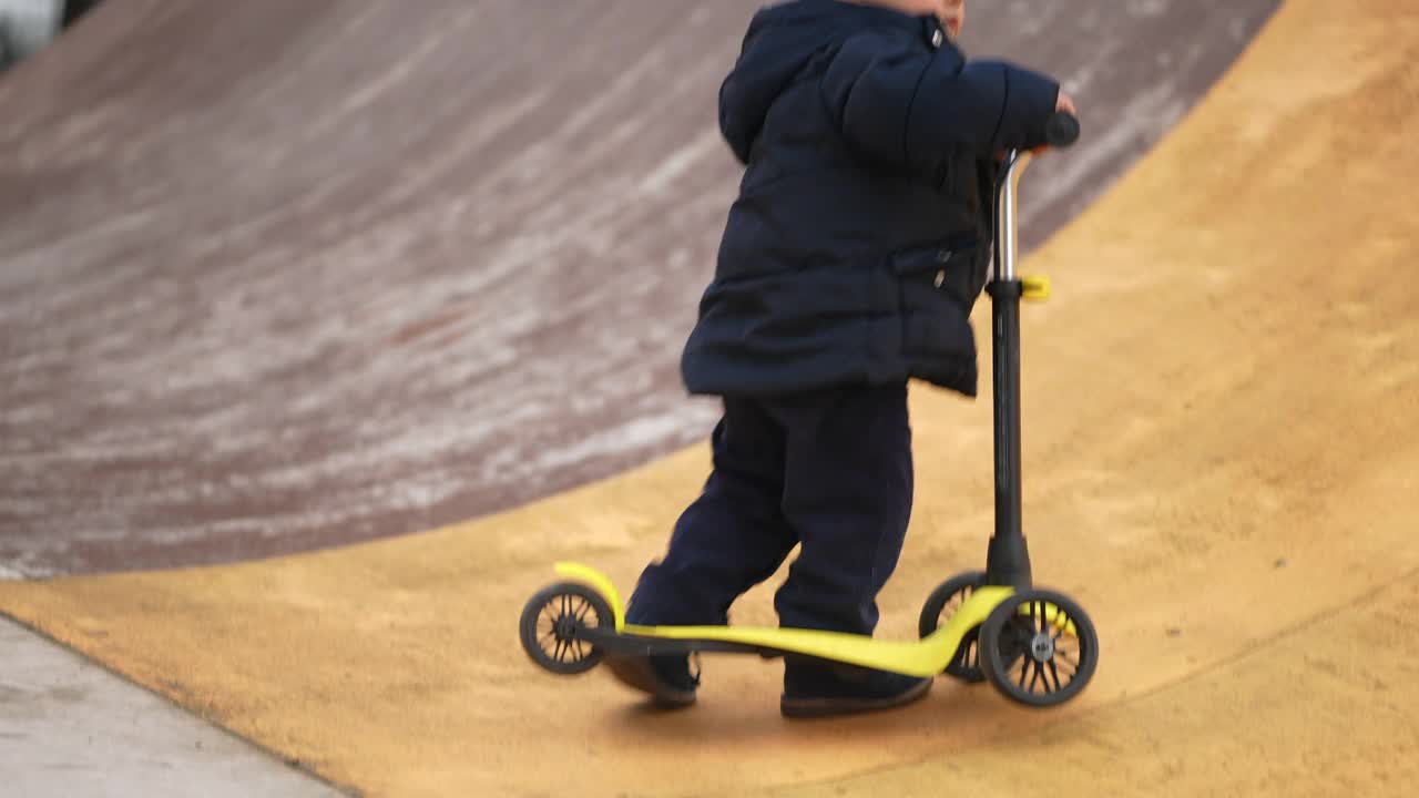 孩子骑玩具滑板车。蹒跚学步的孩子骑着三轮车视频素材