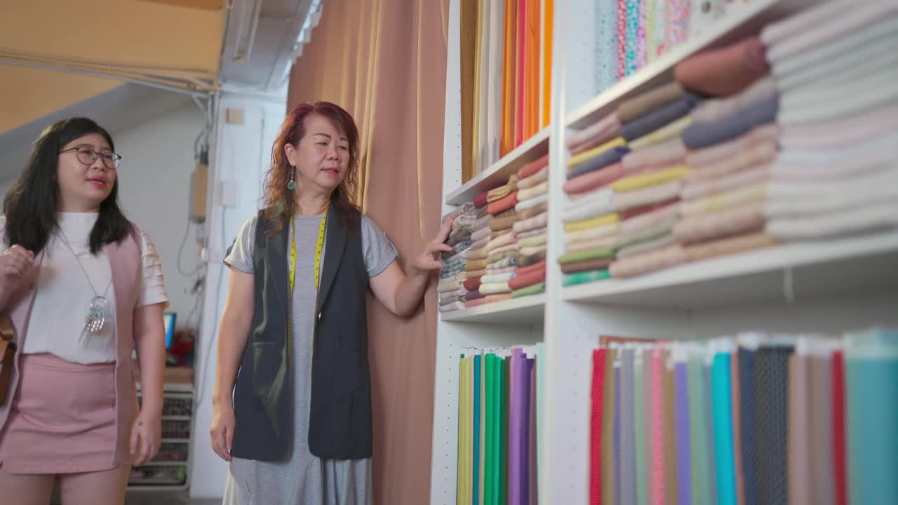 亚洲华裔高级女性裁缝挑选和展示她的顾客在面料服装选择和新的定制服装建议在她的商店视频素材