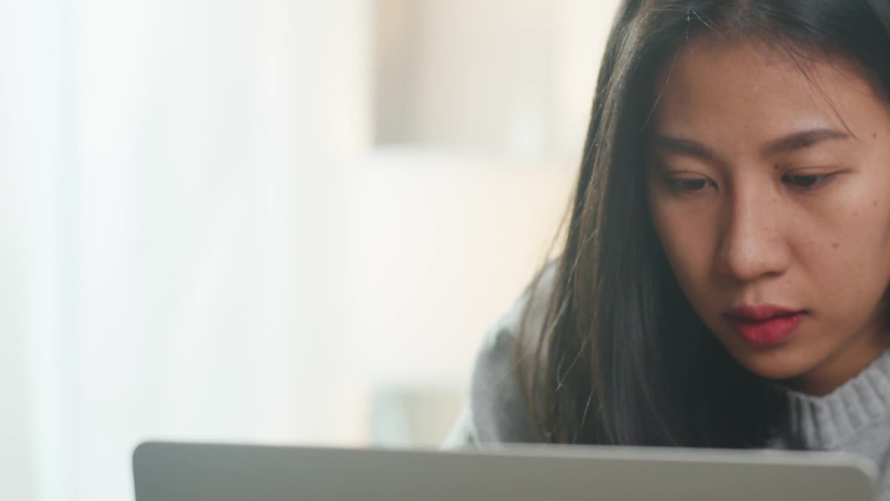 自由职业者亚洲女性的肖像穿着便服，在家里的卧室里用笔记本辛勤工作。视频素材