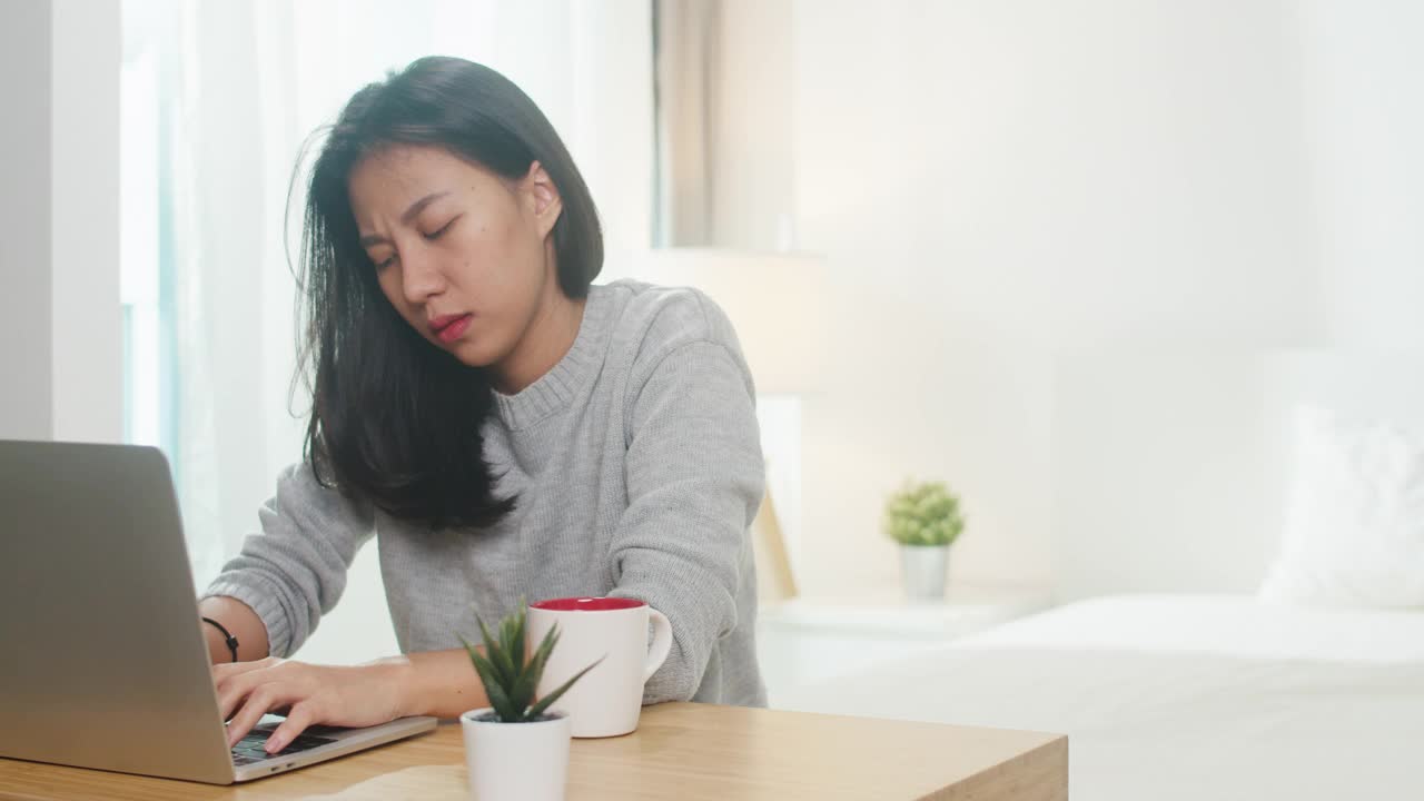 自由职业者亚洲女性的肖像穿着便服，在家里的卧室里用笔记本辛勤工作。视频素材