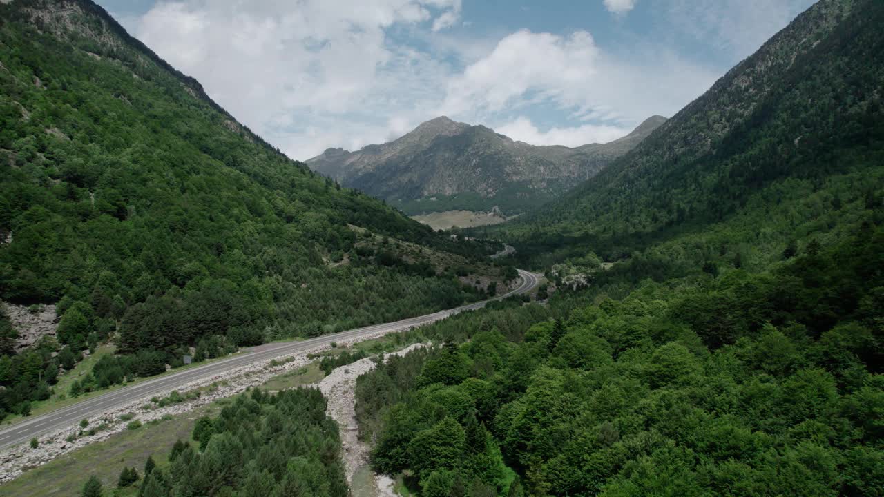 美丽的无人机视野的沥青公路在高山上。山脉消失在天空中，天空有些许阴云，但山峰被阳光照亮。视频素材