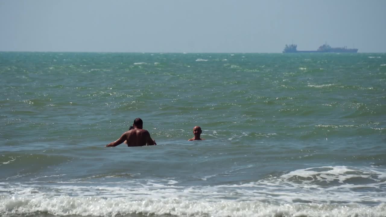 在波涛汹涌的大海中，人们站在浅水里，在大浪中沐浴视频素材