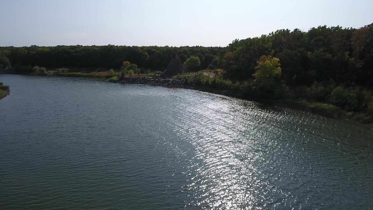 阳光刺眼地照射在河面上。湖岸边的树木。无人机的观点视频素材