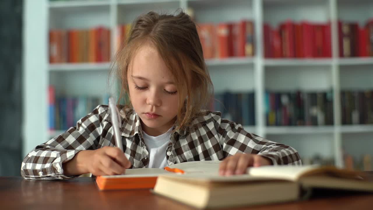 一名白人小学女孩坐在书桌前用铅笔写笔记本做作业的特写照片。视频素材