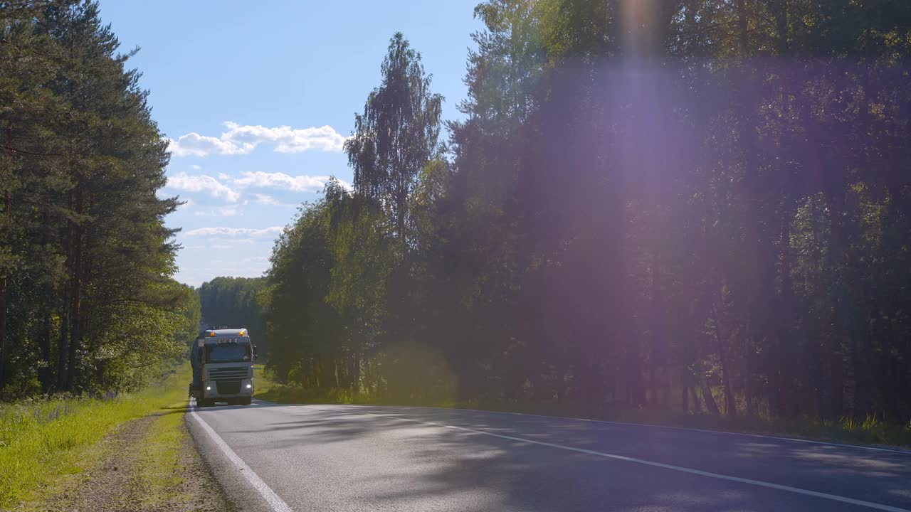 在穿越森林的公路上，一辆半卡车正开着车，载着货物视频素材