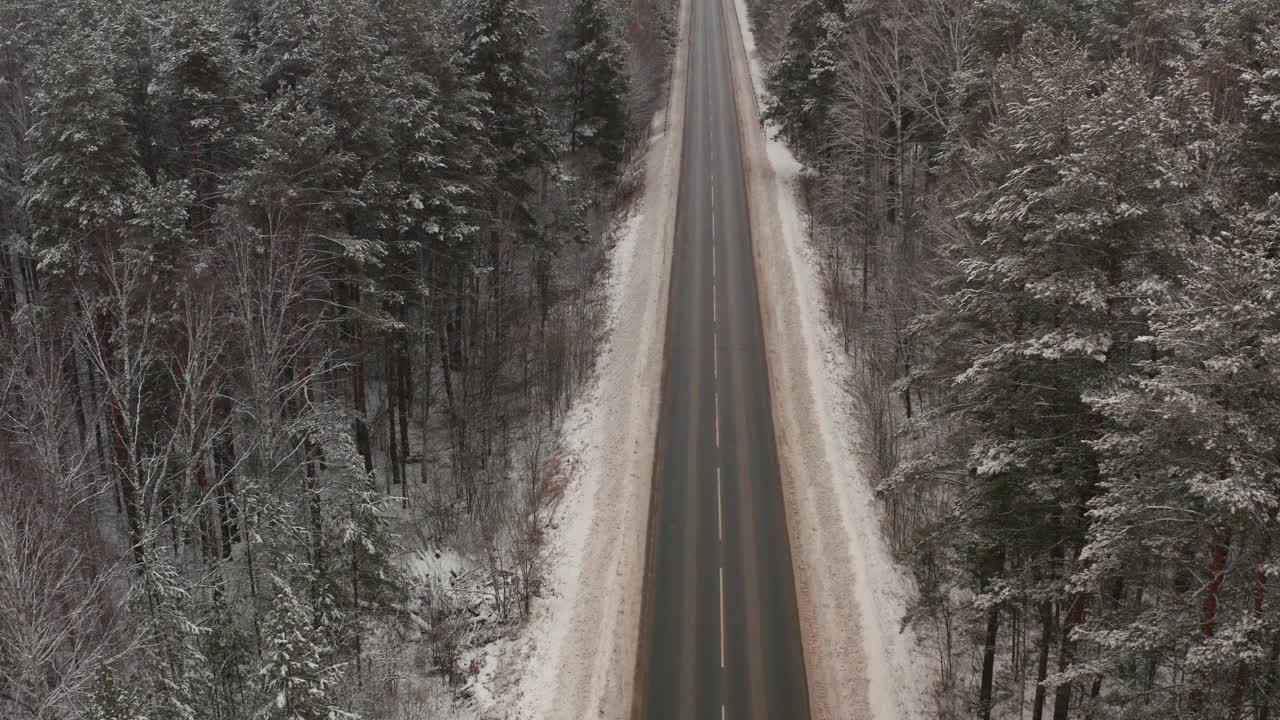 汽车行驶在白雪覆盖的跑道上，俯视图。冬日的道路在寒冷的清晨穿过厚厚的冰冻的树木视频素材