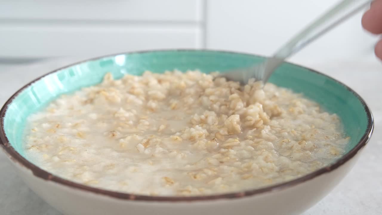 绿色的碗里用勺子搅拌煮好的燕麦粥，健康的早餐和节食产品，美味的素食视频素材