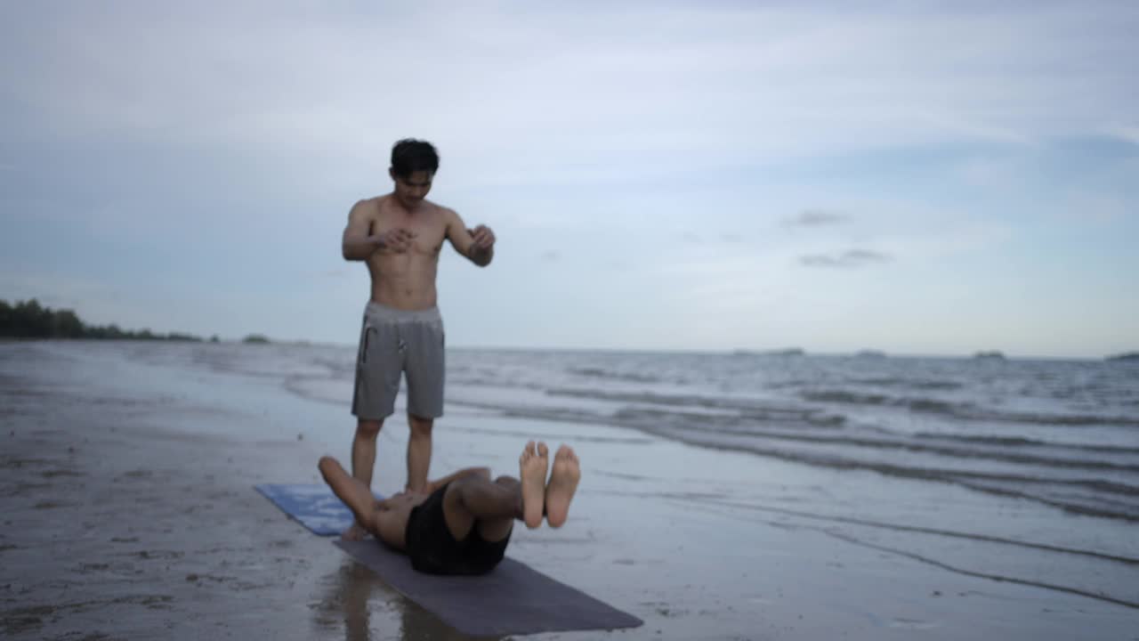 年轻的肌肉强壮的亚洲人锻炼场景日落在海滩上。视频素材