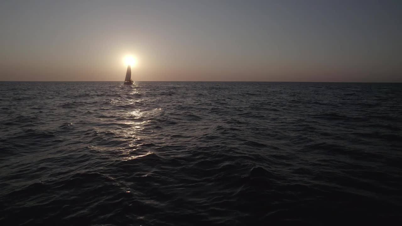 日出的海面上，摄像机飞过水面。一艘帆船在天空中缓缓航行。视频素材