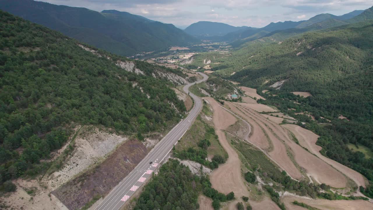 美丽的无人机视野的沥青公路在高山上。山脉消失在天空中，天空有些许阴云，但山峰被阳光照亮。视频素材