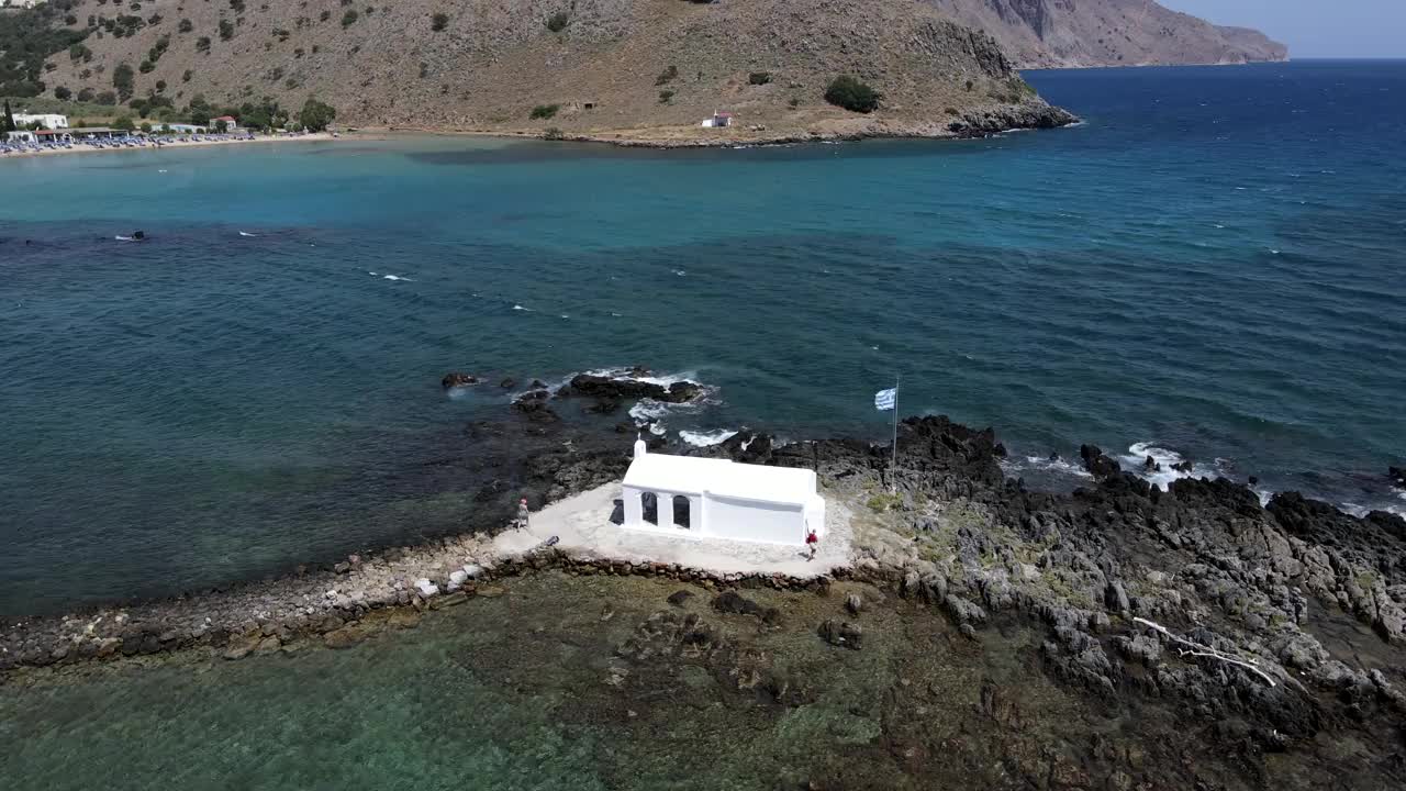 无人机视图在岩石海岸上白色的礼拜堂对希腊国旗和大海的背景。视频素材