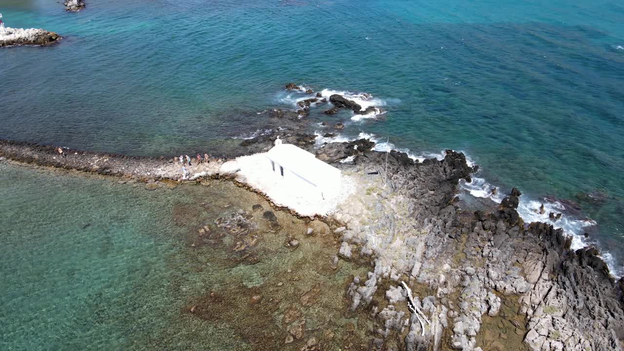 无人机视野在岩石海岸上的白色教堂，背景是蓝绿色的海水。视频素材