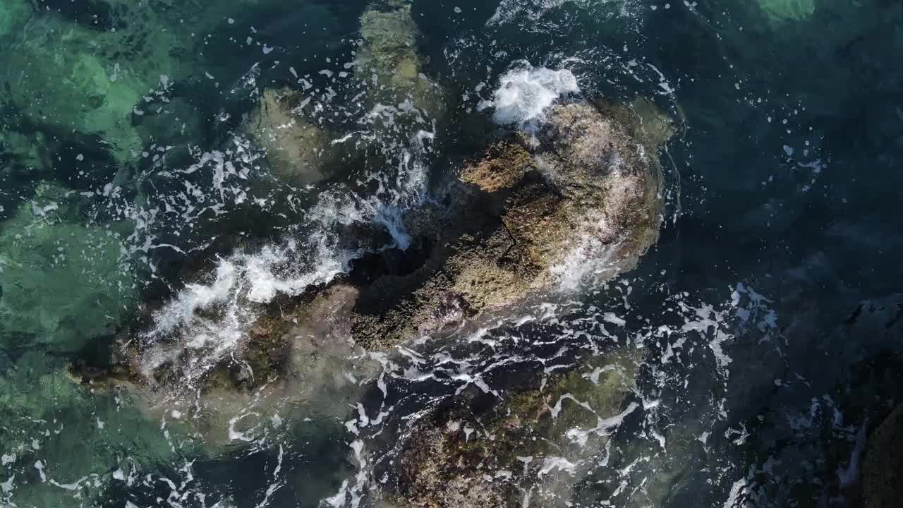 无人机在蓝绿色的海水，海浪，飞溅，泡沫和岩石上的视图。视频素材