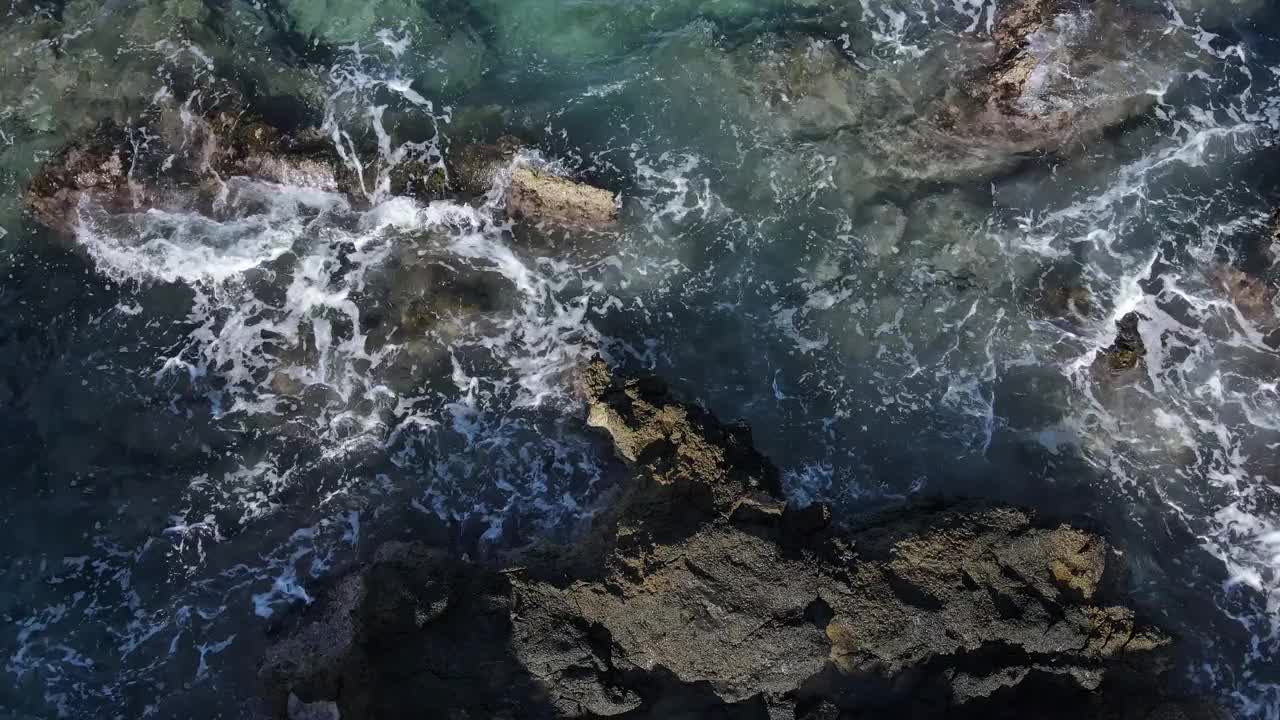 无人机在蓝绿色的海水，海浪，飞溅，泡沫和岩石上的视图。视频素材