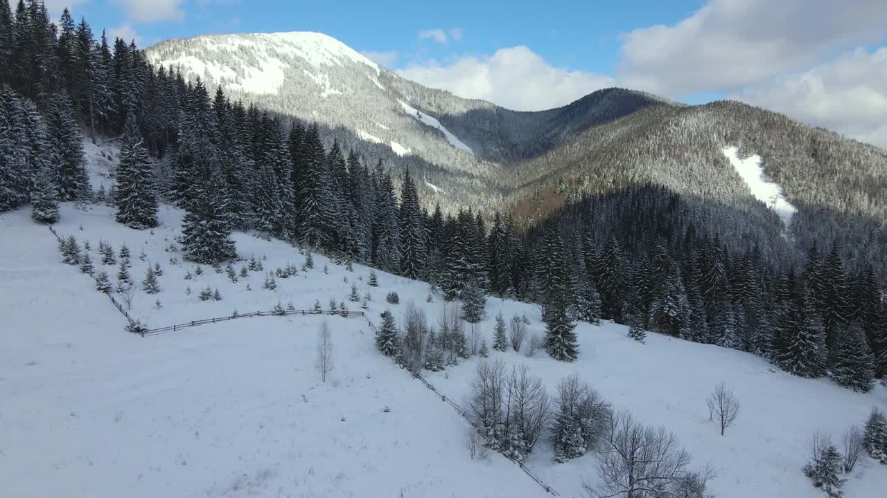 空中冬季景观与小乡村房屋之间的雪覆盖森林在寒冷的山。视频素材