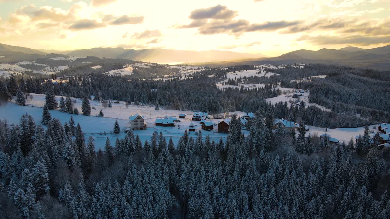 空中冬季景观与小村庄房屋之间的雪覆盖森林在寒冷的山在晚上。视频素材