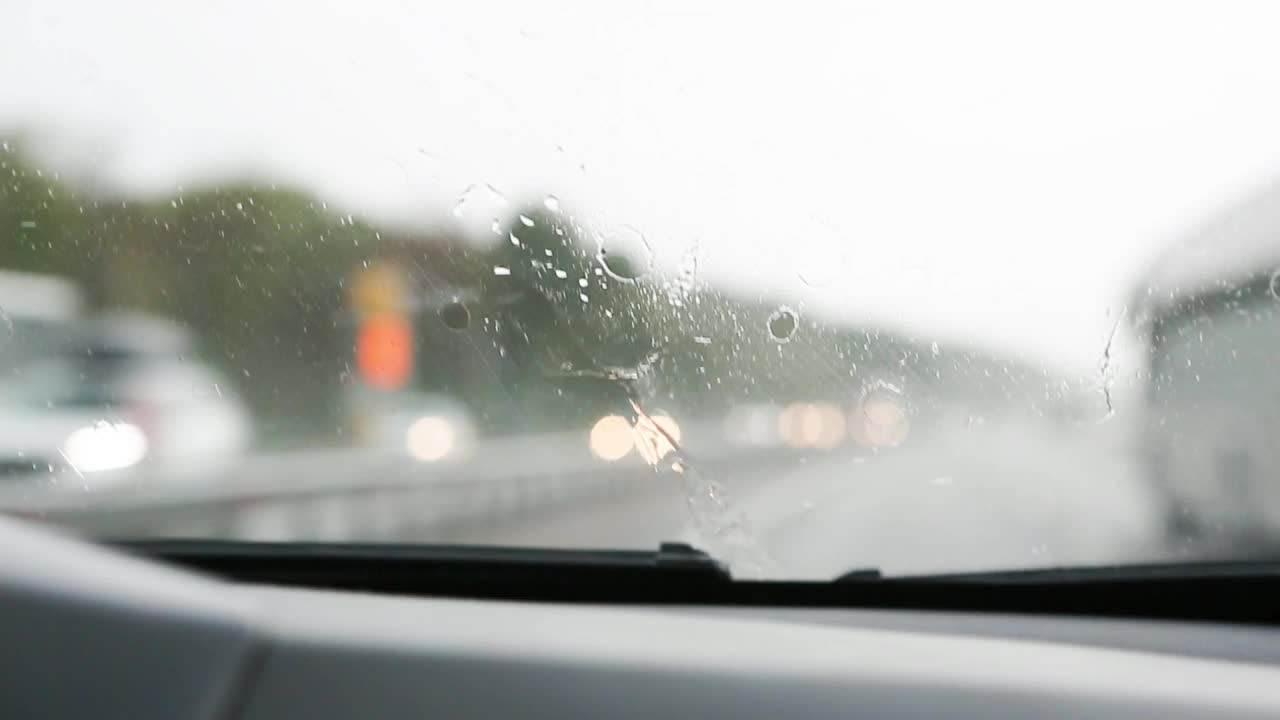 在能见度有限的情况下驾驶汽车:大雨，雨刷清洁挡风玻璃。高速公路上迎面而来的车辆开着前灯。恶劣天气条件下的道路安全。从车内看视频素材