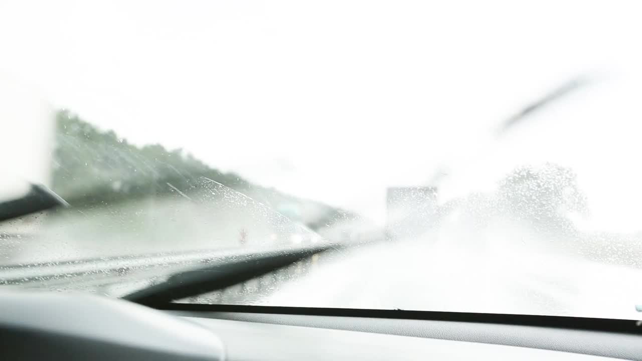 在能见度有限的情况下驾驶汽车:大雨，雨刷清洁挡风玻璃。高速公路上迎面而来的车辆开着前灯。恶劣天气条件下的道路安全。从车内看视频素材