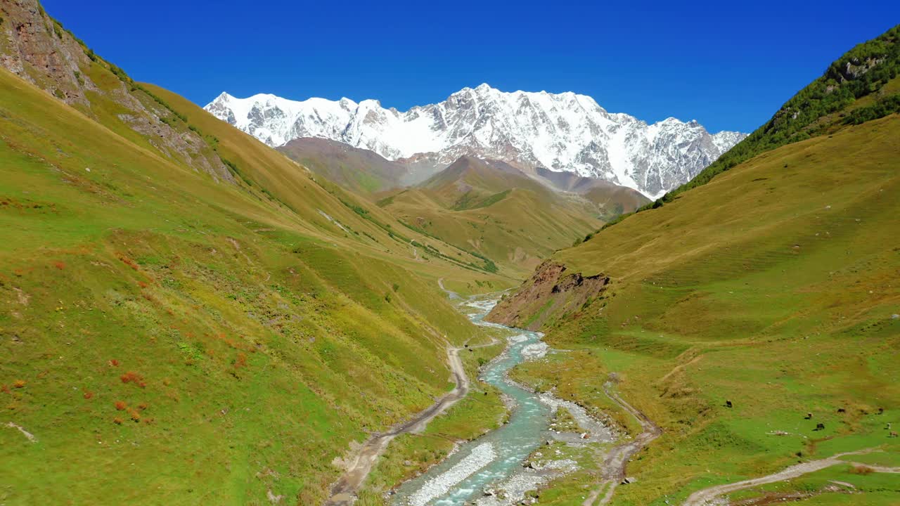 鸟瞰图的一条河在一个山谷的背景积雪覆盖的山脉。视频素材