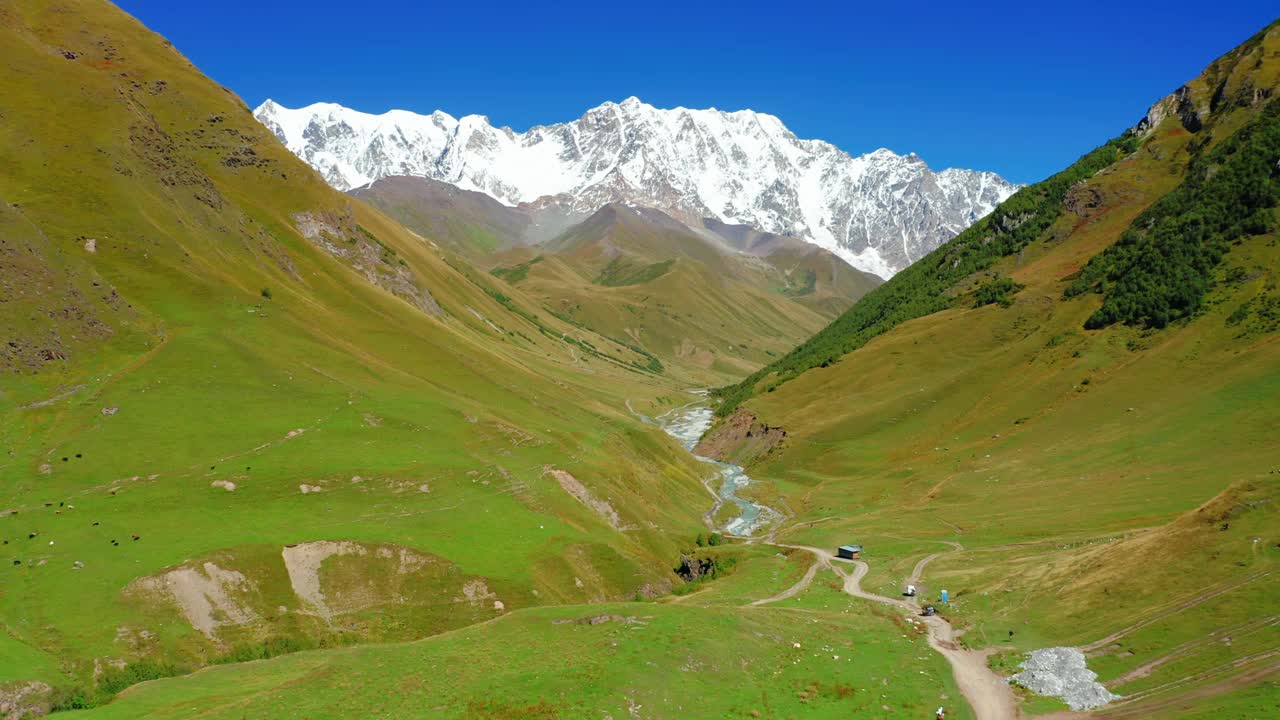 鸟瞰图的道路在一个山谷的背景积雪覆盖的山脉。视频素材