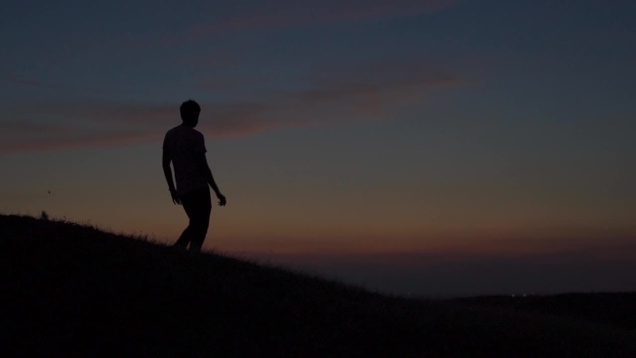 一个印度人的剪影，在蓝色的时间里，夕阳西下，走在橙色的云前。孤独的人走在橘色的云前。孤独的背景。视频素材