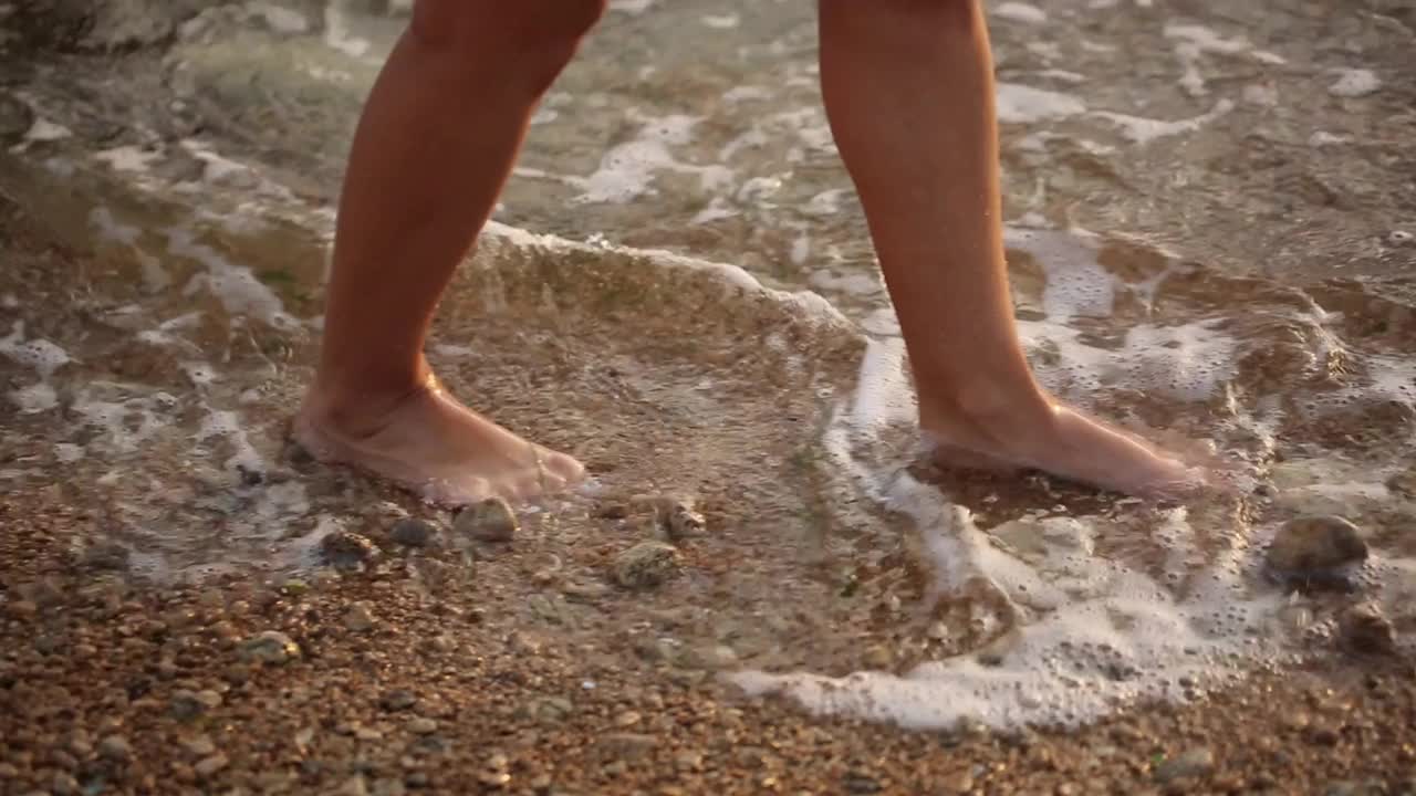 女人的脚赤脚在泡沫的海洋，海浪的海滩上，夏天的一天接近视频下载