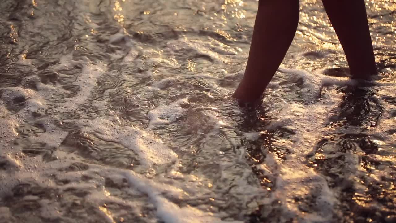 女人的脚赤脚在泡沫的海洋，海浪的海滩上，夏天的一天接近视频下载