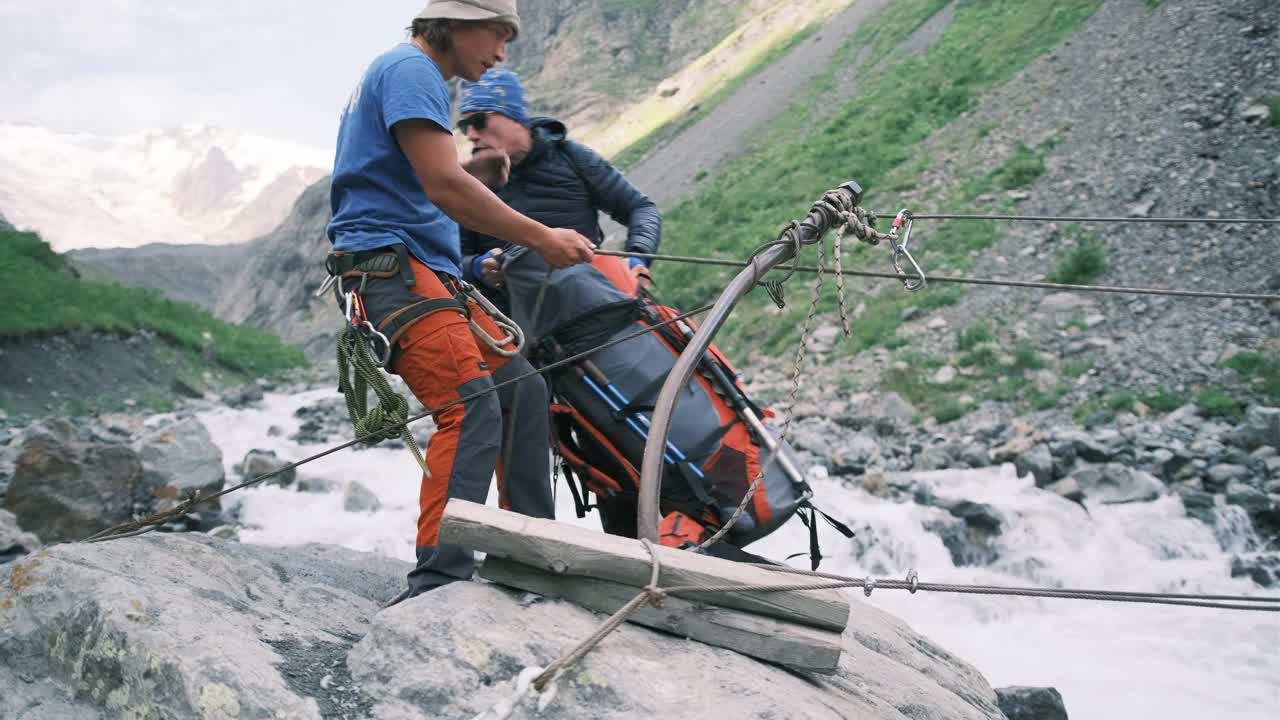 一群游客在徒步旅行中通过绳索穿越一条湍急的山河。视频素材