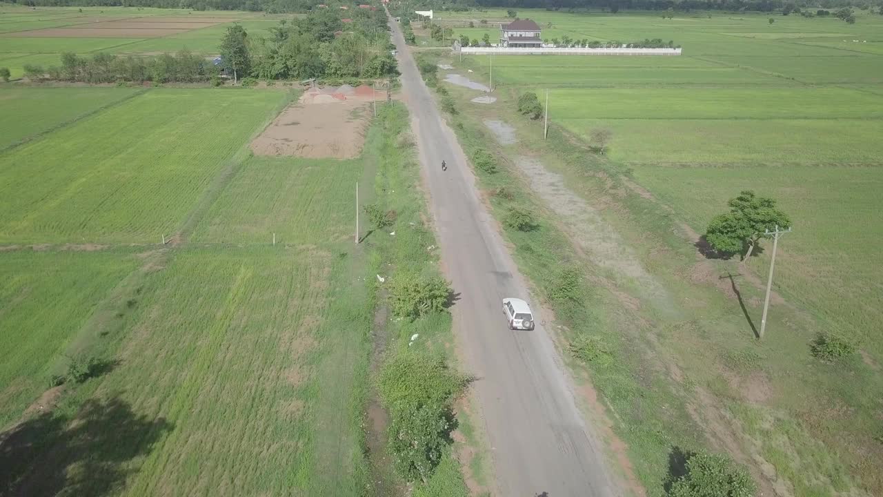 飞过摩托车和车辆行驶在被稻田包围的乡村道路上视频素材