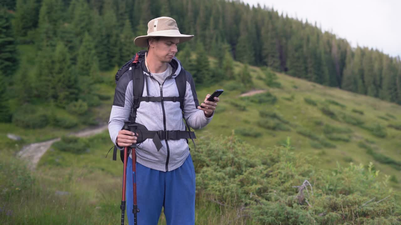 一名游客背着旅游背包站在山顶上，手里拿着智能手机在打电话。移动网络覆盖概念。视频素材