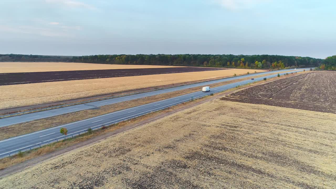 日落时分，卡车在田野间的公路上行驶。卡车行驶在一条笔直的道路上，在日落俯视图视频素材