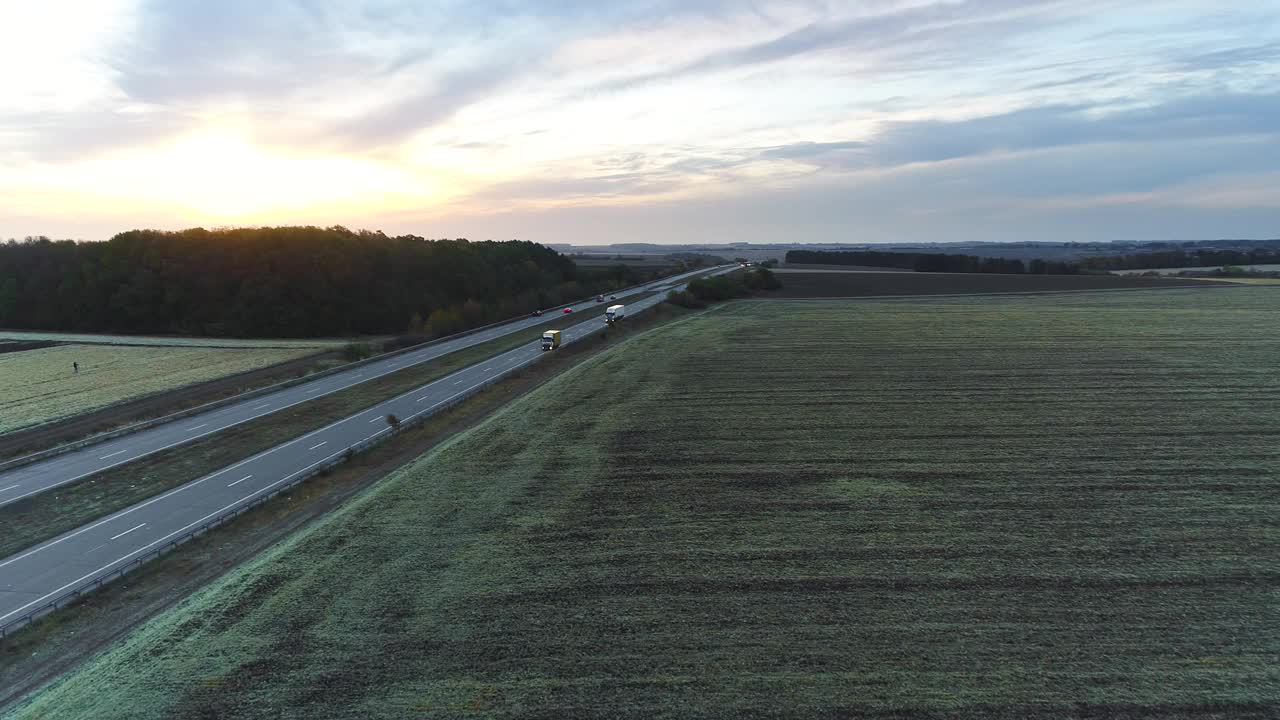 日落时分，卡车在田野间的公路上行驶。卡车行驶在一条笔直的道路上，在日落俯视图视频素材