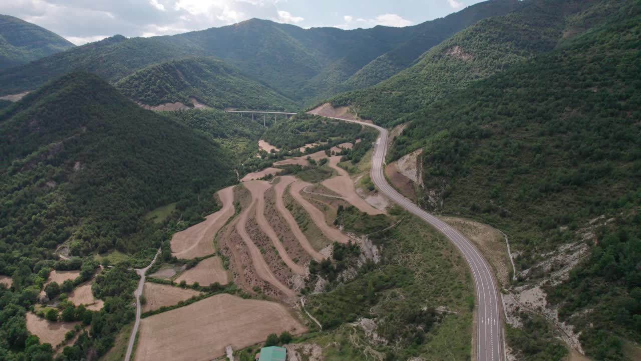 美丽的无人机视野的沥青公路在高山上。山脉消失在天空中，天空有些许阴云，但山峰被阳光照亮。视频素材