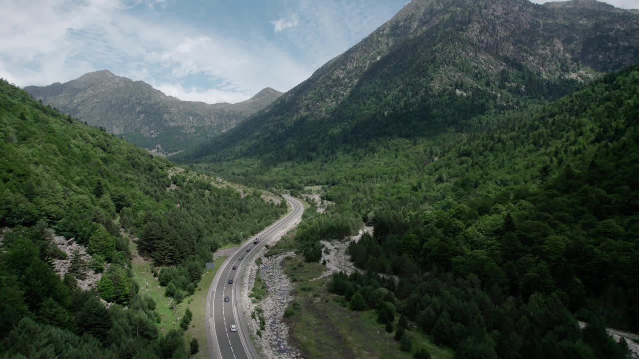 美丽的无人机视野的沥青公路在高山上。山脉消失在天空中，天空有些许阴云，但山峰被阳光照亮。视频素材