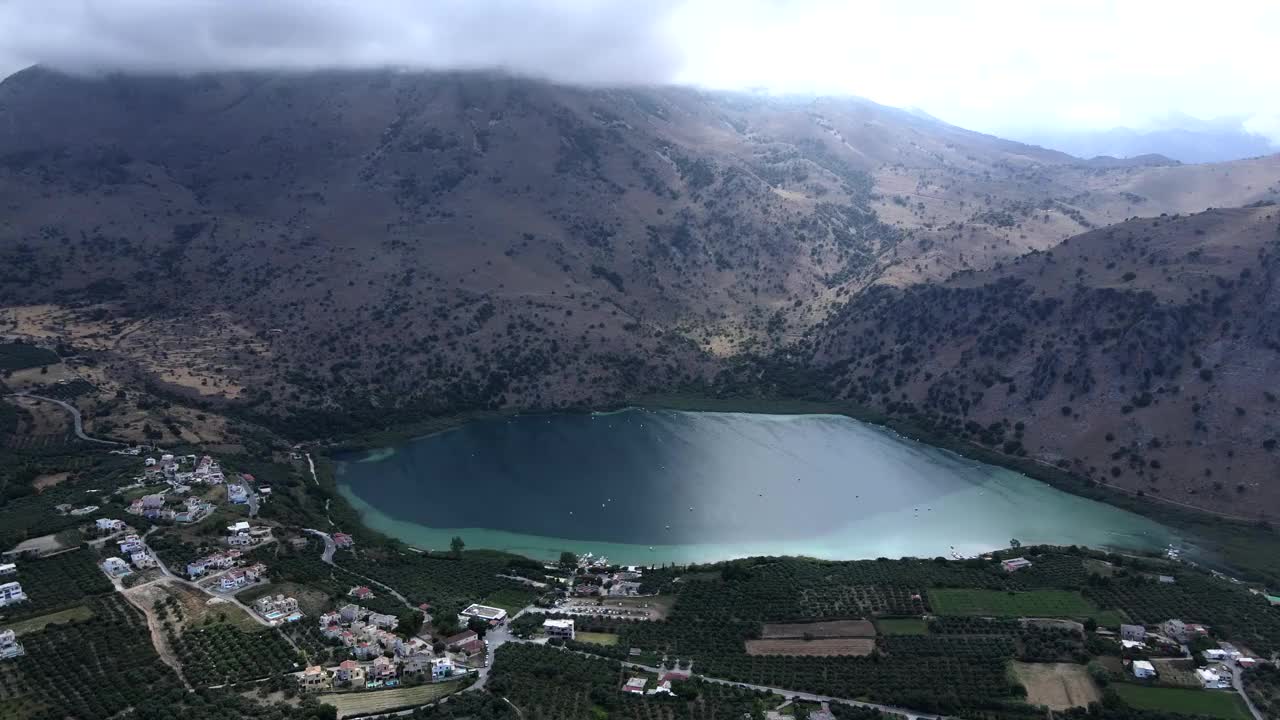 无人机在湖中、水上漂浮的双体船、克里特岛上的村庄和山脉。视频素材