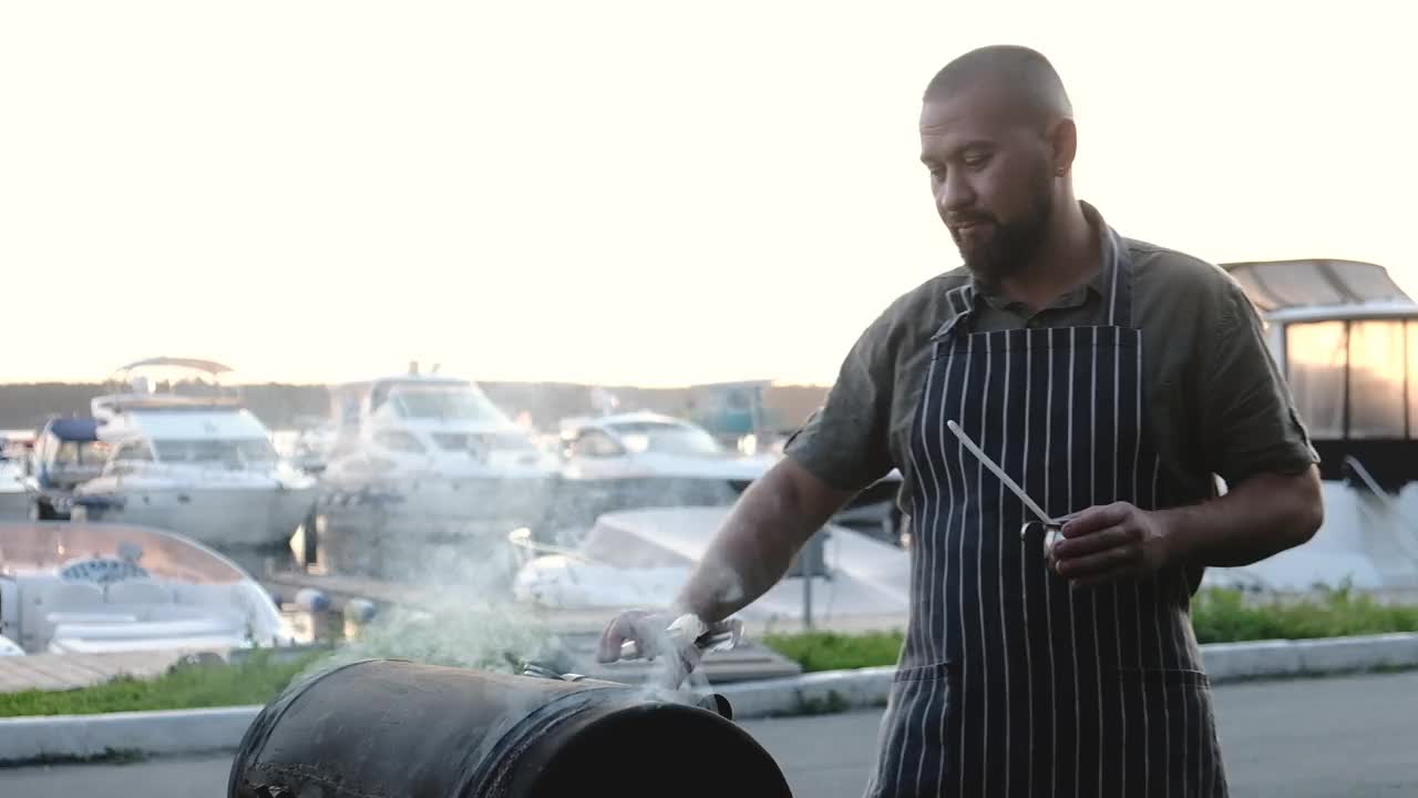 烤肉的人打开金属烤架，用钳子把肉涂上油视频素材