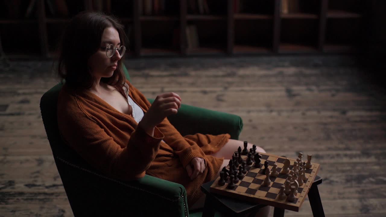 严肃睿智的女棋手戴着眼镜，坐在暗室里下棋走棋。视频素材