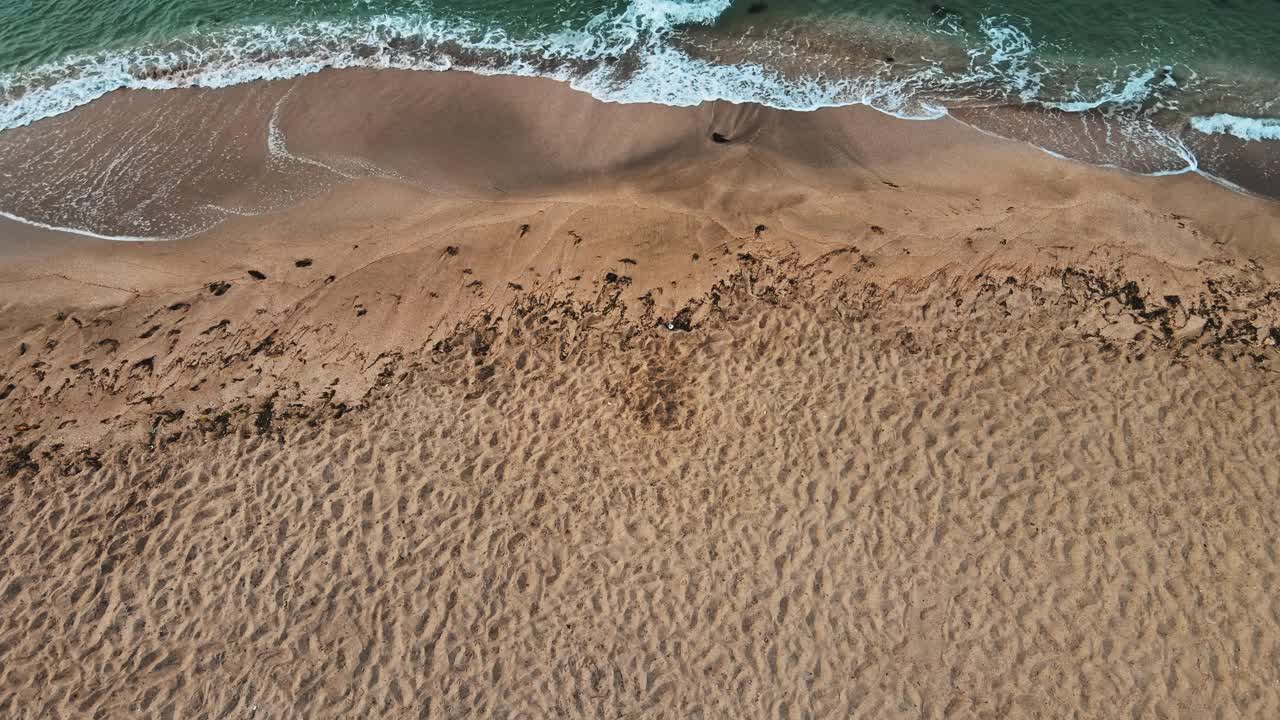 无人机在美丽的海滩上空飞行的鸟瞰图，从顶部角度可以看到海浪和海浪拍打在沙滩上的景象视频素材