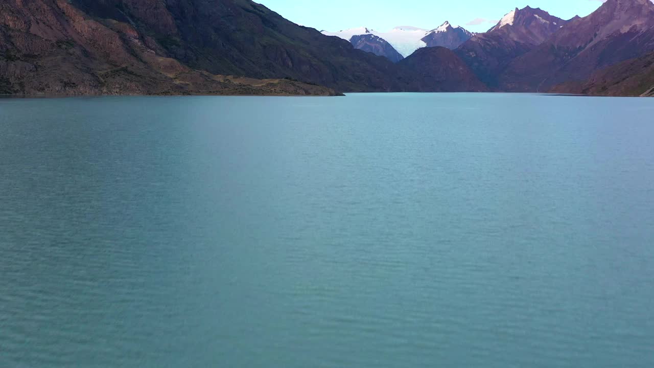 航拍:雪山在多云的天空下的风景，无人机在湖上飞行前进-巴塔哥尼亚，智利视频素材